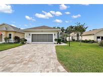 Charming single-story home with a well-maintained lawn and brick driveway under a blue sky at 3584 Tropical Seas Loop, Tavares, FL 32778