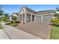 Beautiful home features a two-car garage, brick paved driveway, stone accents, and manicured landscaping at 8272 Procida Isle Ln, Windermere, FL 34786