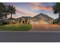 Sprawling one-story home with a 3-car garage and mature palm trees in a landscaped front yard at sunset at 1721 Sunset Ridge Dr, The Villages, FL 32162