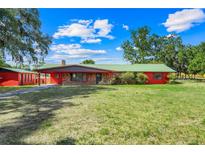 Charming red brick home featuring a green metal roof, lush lawn, and mature shade trees at 274 W Kings Hwy, Center Hill, FL 33514