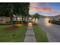 Charming home featuring a manicured lawn, mature trees, and a walkway leading to the front door at 506 Weston Manor Dr, The Villages, FL 32162