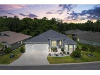 Beautiful single-story home with a well-manicured lawn, mature trees, and a three-car garage at 6988 Lawrenceville Way, The Villages, FL 34762