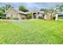 Spacious landscaped front yard with verdant lawn and charming tan home with arched entryway at 11301 Via Mari Cae Ct, Clermont, FL 34711