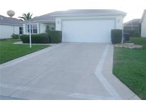 Home with two-car garage, driveway, trimmed hedges, and well manicured green grass at 1310 Jimenez Ct, The Villages, FL 32159