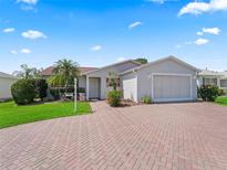Charming single-story home featuring a two-car garage, brick driveway, well-maintained lawn, and tidy landscaping at 3266 Woodridge Dr, The Villages, FL 32162