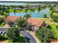 Stunning aerial view of townhomes with terracotta roofs overlooking a tranquil lake and lush green landscape at 5492 Compass Pt, Oxford, FL 34484
