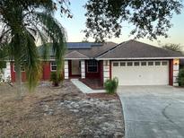 Charming red home with solar panels, a two-car garage, and well-maintained landscaping at 808 Chamberlain Loop, Lake Wales, FL 33853