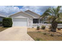 Charming home featuring a well-maintained lawn, a white picket fence, and a two-car garage at 971 Margaux Trl, The Villages, FL 32162