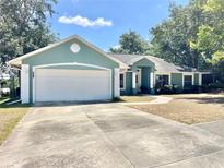 Charming one-story home with a two-car garage and green exterior paint, nestled among mature trees and a well-kept front yard at 974 Forest Hill Dr, Minneola, FL 34715
