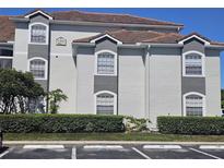 Exterior view of condo building with gray accents, a red tile roof, and well-maintained landscaping in a parking lot at 14049 Fairway Island Dr # 118, Orlando, FL 32837