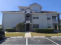 A three-story condo building features gray exterior paint, white stairs, and lush green landscaping with a parking lot at 14049 Fairway Island Dr # 118, Orlando, FL 32837
