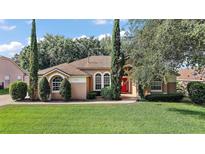 Charming single-story home with a well-manicured lawn, mature trees and a lovely red front door at 14624 Pine Lake St, Clermont, FL 34711