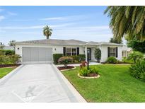 Charming single-story home featuring a manicured lawn, mature landscaping, and a concrete driveway with a unique design at 2022 Claudio Ln, The Villages, FL 32159
