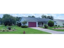 Charming single-story home with a well-manicured lawn, vibrant landscaping, and a brick-paved driveway leading to a purple garage door at 25800 Belle Helene, Leesburg, FL 34748