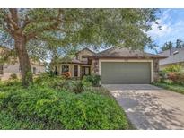 Charming home with lush landscaping and a stone-accented facade and a two-car garage, all shaded by a mature tree at 8167 Bridgeport Bay Cir, Mount Dora, FL 32757