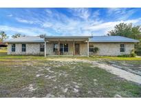 Charming single-story brick home with a metal roof and covered front porch with beautiful blue skies above at 9236 County Road 48, Yalaha, FL 34797