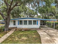 Charming single-story home with a wooden deck and a covered carport, framed by mature trees and a green lawn at 2110 Oak Cir, Mount Dora, FL 32757