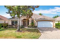 Charming single-story home featuring a lush front yard, arched entryway, and a brick paved driveway leading to a two-car garage at 2202 Kershaw Rd, The Villages, FL 32162