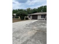 Modest single-story home with a driveway and a one car garage surrounded by landscaping and trees at 2421 Centennial Blvd, Leesburg, FL 34748