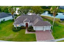 Waterfront home with a brick driveway, mature landscaping, and an attached two car garage at 4879 Brightmour Cir, Orlando, FL 32837