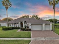 Charming single-story home featuring a three-car garage, lush landscaping, and a brick paver driveway at sunset at 4879 Brightmour Cir, Orlando, FL 32837