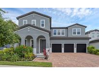 Two-story gray home featuring a brick driveway, a three-car garage, and beautiful landscaping at 14513 Winter Stay Dr, Winter Garden, FL 34787