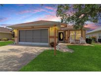 Charming single-story home featuring a screened garage, welcoming front porch with rocking chairs, and a well-manicured lawn at 21646 Stirling Pass, Leesburg, FL 34748