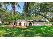 Charming white stucco home with arched entryway and mature trees offers shade and curb appeal at 6750 Sunnyside Dr, Leesburg, FL 34748