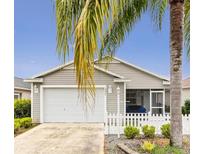 Charming single-story home featuring a white picket fence, a two-car garage, and a screened in front porch at 2457 Upton St, The Villages, FL 32163