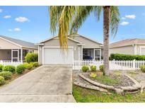 Charming single-story home featuring a well-manicured lawn, white picket fence and an attached garage at 2457 Upton St, The Villages, FL 32163