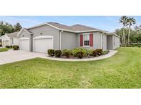 A modern one-story home with a gray exterior, two-car garage, and a well-manicured lawn with shrubbery at 27215 White Plains Way, Leesburg, FL 34748