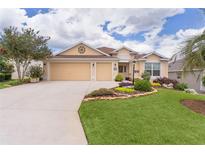 Charming home with manicured front lawn, mature trees, and a two-car garage under a sunny blue sky at 627 Leeds Pl, The Villages, FL 32162