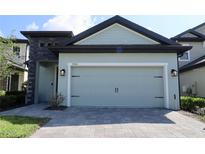 Two car garage with blue paint, black accents and a gray brick driveway on a sunny day at 7955 Delwin Ln, Reunion, FL 34747