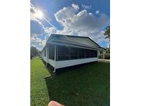 Side view of a home featuring a screened-in porch, nice green grass and sunny skies at 1005 Matthew Ave, Lady Lake, FL 32159