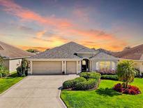 Charming single-story home boasting a three-car garage, lush landscaping, and inviting curb appeal at sunset at 1304 Zombar Pl, The Villages, FL 32163