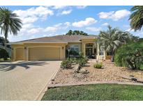 Beautiful home with a three-car garage, tan exterior, desert landscaping, and a brick paved driveway at 2204 Baypoint Way, The Villages, FL 32162