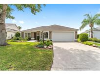 Charming single-story home featuring a two-car garage, manicured lawn and mature trees under a bright blue sky at 467 Weston Manor Dr, The Villages, FL 32162