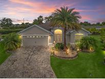 Charming home with landscaped yard, stone driveway, and a beautiful palm tree at dusk at 631 Independence Path, The Villages, FL 32163