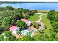 Expansive aerial view of estate, pool, and waterfront, with a red-roofed white home surrounded by lush greenery at 9023 Silver Lake Dr, Leesburg, FL 34788