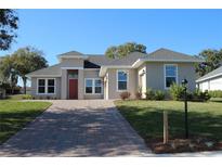 Charming one-story home with a brick driveway, well-manicured lawn, and inviting red front door at 0 Spinnaker Loop, Lady Lake, FL 32159