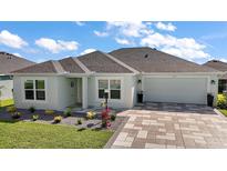 Charming home featuring a manicured lawn, paver driveway, and coordinated landscaping at 1627 Mclucas Ln, The Villages, FL 34762