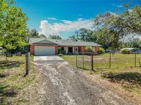 Charming brick home with a well-maintained lawn, gated driveway, and a two-car garage at 27610 Debbie Rd, Okahumpka, FL 34762