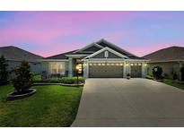 Charming single-story home with well-manicured lawn, three car garage, and neutral palette under a dramatic pink and purple sky at 6243 Danielson Loop, The Villages, FL 32163