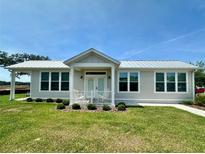 Charming single story home with a metal roof, a manicured lawn, and a quaint front porch at 12077 Lakeshore Way, Oxford, FL 34484