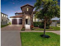 Beautiful home exterior with stone accents, a well-manicured lawn, and a brick driveway leading to a two-car garage at 14907 Guava Bay Dr, Winter Garden, FL 34787