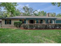 Charming brick home with dark shutters, a manicured lawn, and mature trees at 18015 Palm St, Umatilla, FL 32784