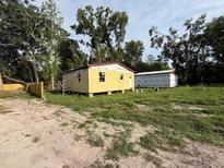 Charming yellow home exterior with a large lawn surrounded by lush trees under a bright sky at 352 S Justice, Bushnell, FL 33513
