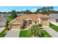 Beautifully landscaped, this tan home features an eye-catching red front door and a convenient three-car garage at 4716 Heritage Trl, Leesburg, FL 34748