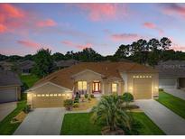 Beautifully landscaped, this tan home features an eye-catching red front door and a convenient three-car garage at 4716 Heritage Trl, Leesburg, FL 34748