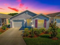 Charming single-story home with a well-manicured lawn, lush shrubs, and a vibrant, colorful sky at dusk at 865 Conroe St, The Villages, FL 34762